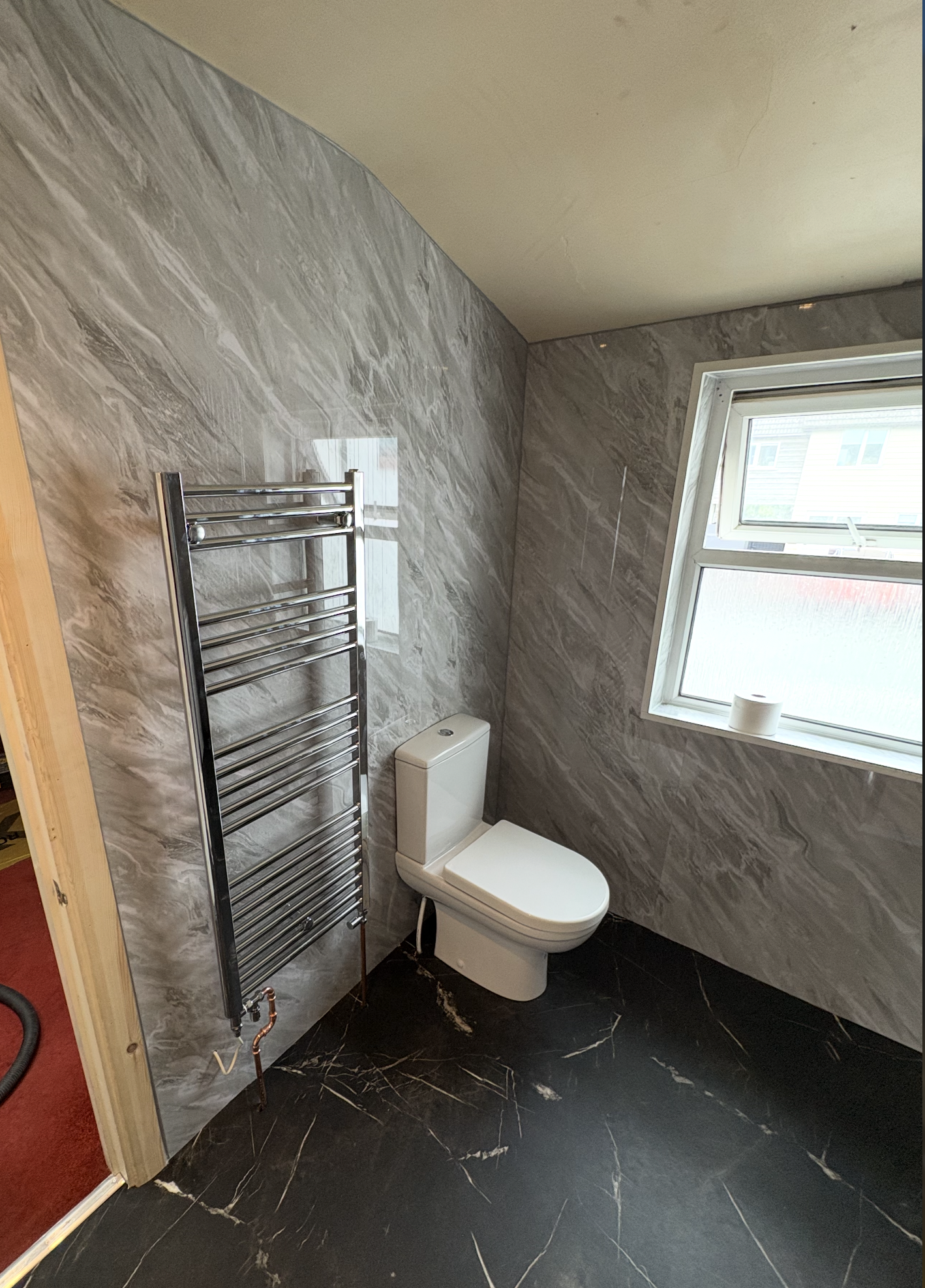 Bathroom after CR Plumbing refit — grey marble panels, black floor and chrome towel rail